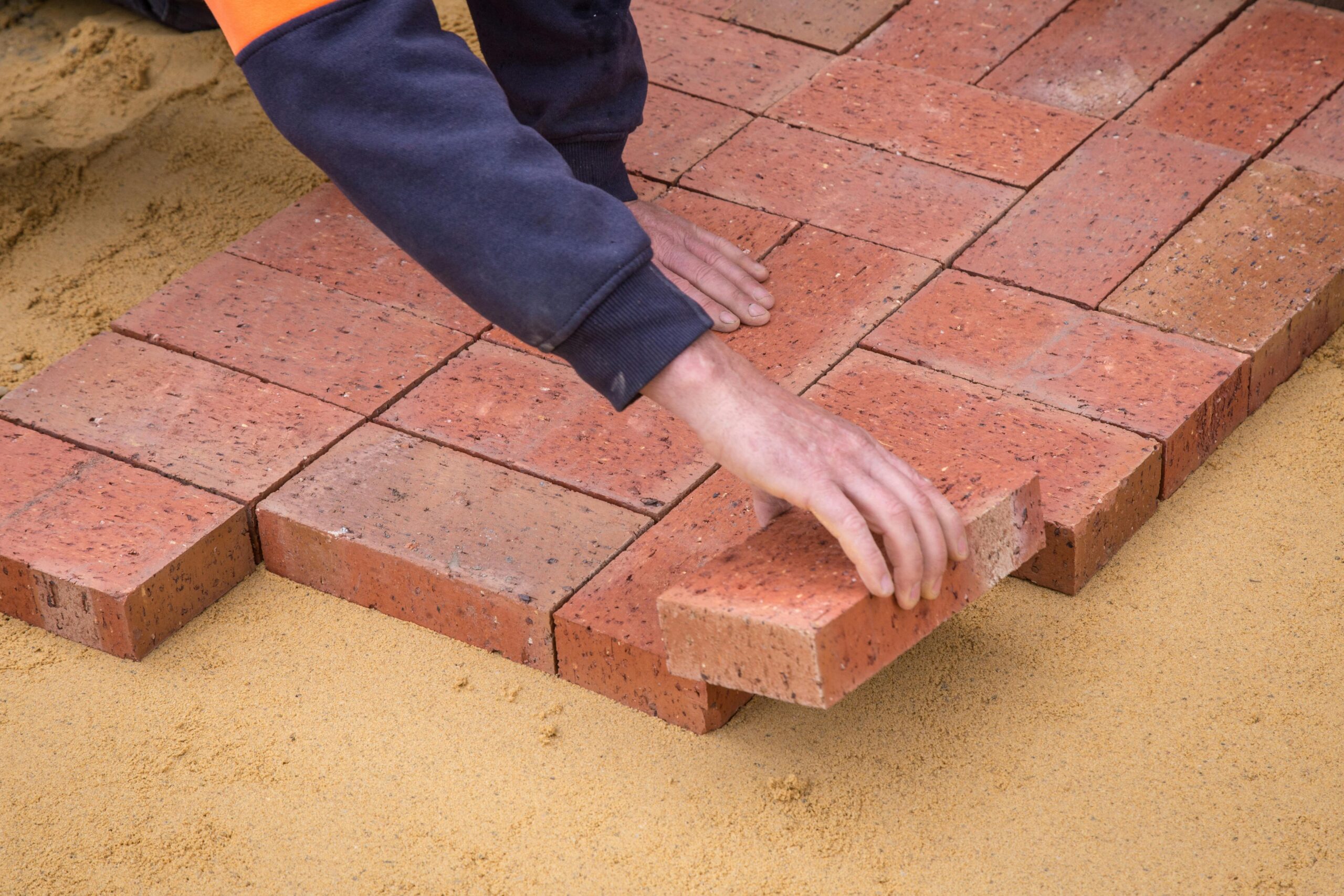 Home Worker's hand laying red bricks on sand for pavement construction.